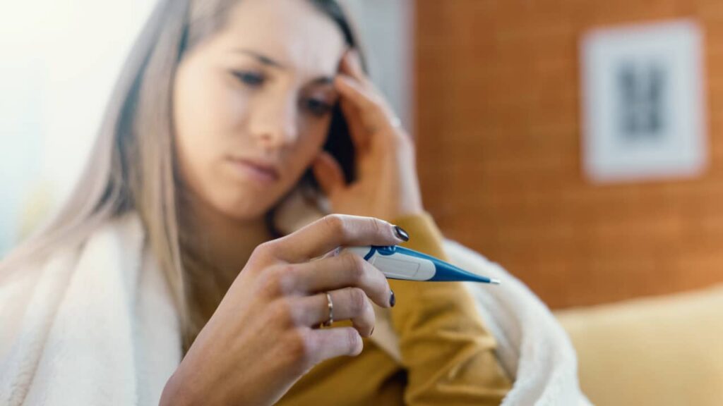 Ill Woman checking her temperature with thermometer